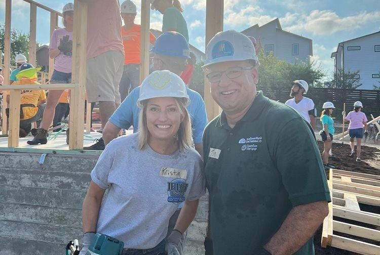 Two people with hard hats volunteering outside building houses